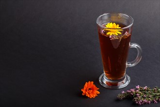 Glass of herbal tea with calendula and hyssop on a black background. Morninig, spring, healthy