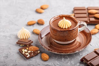 Cup of hot chocolate and pieces of milk chocolate with almonds on a gray concrete background. side