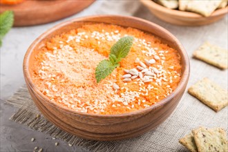 Carrot cream soup with sesame seeds and snacks in wooden bowl on a gray concrete background with