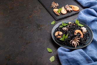 Black cuttlefish ink pasta with shrimps or prawns and small octopuses on black concrete background