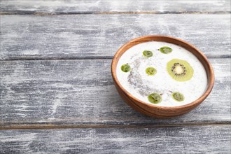 Yogurt with kiwi, gooseberry, chia and almonds in wooden bowl on gray wooden background. side view,