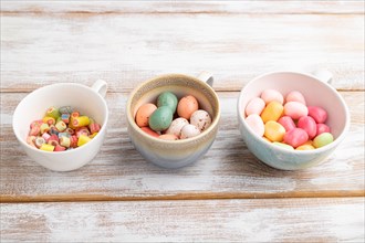 Heap of multicolored caramel candies in cups on white wooden background. copy space, side view,