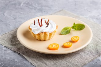 Cake with whipped egg cream on a light brown plate with kumquat slices and mint leaves on a gray