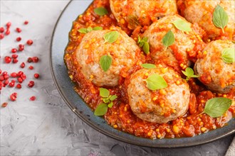 Pork meatballs with tomato sauce, oregano leaves, spices and herbs on blue ceramic plate on a gray