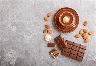 Cup of hot chocolate and pieces of milk chocolate with almonds on a gray concrete background. Flat