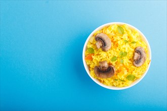 Yellow fried rice with champignons mushrooms, turmeric and oregano in white ceramic bowl on a blue