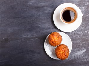 Two carrot muffins with cup of coffee on white plate on black wooden background. top view with