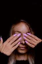 Woman with purple nails covering her eyes, against a dark background radiating calmness