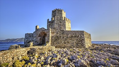 Ruins of a castle on a rocky coast with a clear sky, octagonal medieval tower. Islet of Bourtzi,