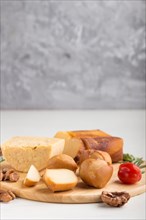 Smoked cheese and various types of cheese with rosemary and tomatoes on wooden board on a gray and
