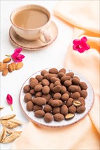 Almond in chocolate dragees on ceramic plate and a cup of coffee on white concrete background and