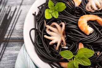 Black cuttlefish ink pasta with shrimps or prawns and small octopuses on gray wooden background and