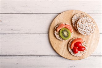 Rice cakes with salmon, kiwi and cherry tomatoes on white wooden background. top view, copy space
