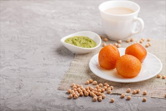 Traditional indian candy gulab jamun in white plate with mint chutney on a gray concrete background