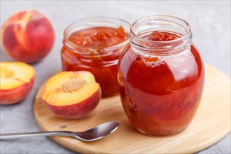 Peach jam in a glass jar with fresh fruits on gray concrete background. side view, close up