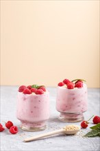 Yoghurt with raspberry and sesame in a glass and wooden spoon on gray and orange background. side