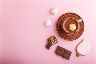 Cup of hot chocolate and pieces of milk chocolate with almonds on pink background. top view, flat