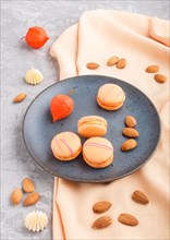 Orange macarons or macaroons cakes on blue ceramic plate on a gray concrete background and orange