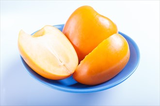 Ripe orange persimmon in a blue plate isolated on white background. closeup