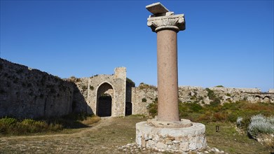 Old antique column in front of ruins with archway and blue sky in the background, sea fortress
