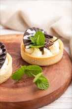 Sweet tartlets with chocolate and cheese cream with cup of coffee on a white wooden background and