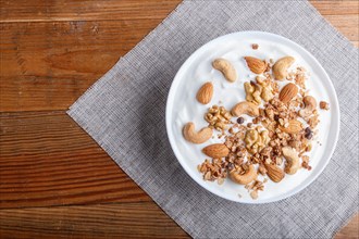 White plate with greek yogurt, granola, almond, cashew, walnuts on brown wooden background. top