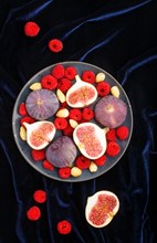 Fresh figs, strawberries and raspberries on blue ceramic plate on black concrete background and