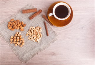A cup of coffee, cinnamon, almonds, hazelnuts, cashew on a linen napkin. Still life. Closeup. copy