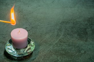 Lit matchstick over lavender candle in glass holder isolated on black textured background