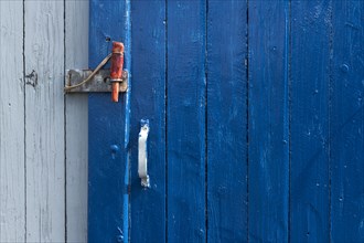 Blue sliding door with handle and red wooden splint to close the wooden wall of a fisherman's hut,