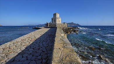 Stone path leads to a castle by the sea under a bright blue sky, octagonal medieval tower. Islet of