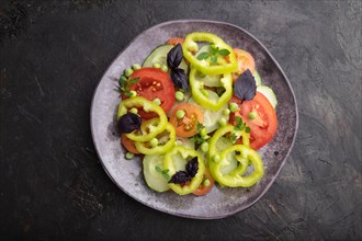 Vegetarian salad from green pea, tomatoes, pepper and basil on a black concrete background. top
