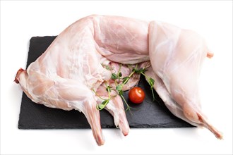 Whole raw rabbit with tomatoes, pea sprouts on a black concrete slate board isolated on white