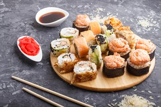 Mixed japanese maki sushi rolls set with chopsticks, ginger, soy sauce, rice on black concrete