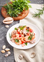 Boiled shrimps or prawns and small octopuses with herbs on white ceramic plate on a black concrete
