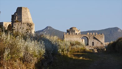 Fortress ruins with overgrown plants and mountains in the background under a blue sky, sea fortress