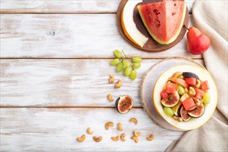 Vegetarian fruit salad of watermelon, grapes, figs, pear, orange, cashew on white wooden background