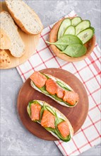 Smoked salmon sandwiches with cucumber and spinach on wooden board on a gray concrete background.