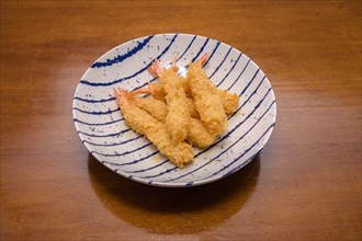 Shrimp tempura on a plate placed against a black background. Tempura is a Japanese food. It is