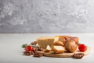 Smoked cheese and various types of cheese with rosemary and tomatoes on wooden board on a gray and