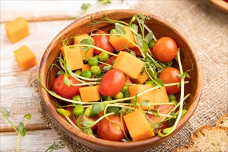 Vegetarian vegetable salad of tomatoes, pumpkin, microgreen pea sprouts on white wooden background