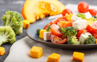 Vegetarian salad with broccoli, tomatoes, feta cheese, and pumpkin on a blue ceramic plate on a