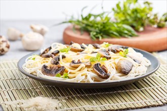 Rice noodles with champignons mushrooms, egg sauce and oregano on blue ceramic plate on a gray