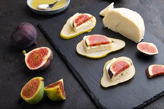 Summer appetizer with pear, cottage cheese, figs and honey on slate board on a black concrete