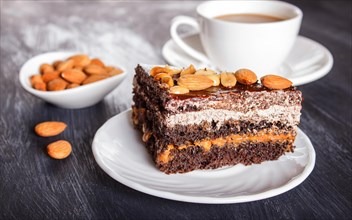 Chocolate cake with caramel, peanuts and almonds on a black wooden background. cup of coffee, close