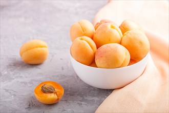 Fresh orange apricots in white bowl on gray concrete background. side view, selective focus