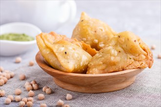 Traditional indian food samosa in wooden plate with mint chutney on a gray concrete background.