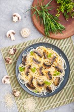 Rice noodles with champignons mushrooms, egg sauce and oregano on blue ceramic plate on a gray