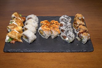 A slate plate hosting a variety of sushi rolls with different toppings and sauces, Majorca,