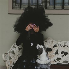Woman with a large black hat playing with a dog on a lace-covered bench